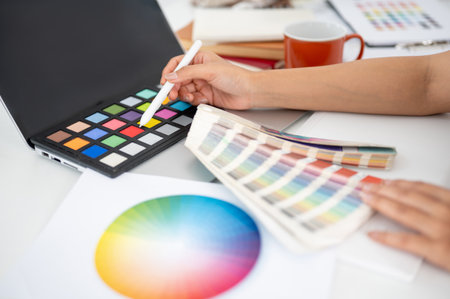 Close up of a hand pointing a stylus at red color on color palette. Choosing or picking a color. Interior Designer or Graphic Designer working in office.の写真素材