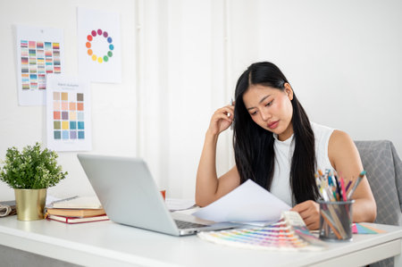 An asian woman is calmly reading through the documents about design color on her working desk. Interior Designer or Graphic Designer working in office.の写真素材