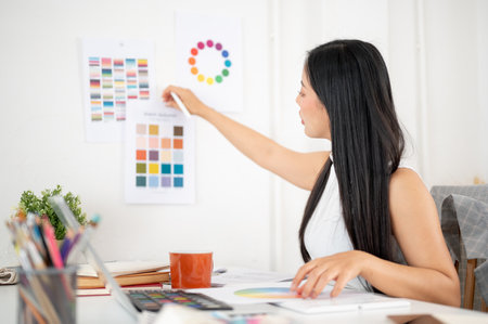 An asian woman is sticking or taking off a printed color palette on the wall. Interior Designer or Graphic Designer working in office.の写真素材