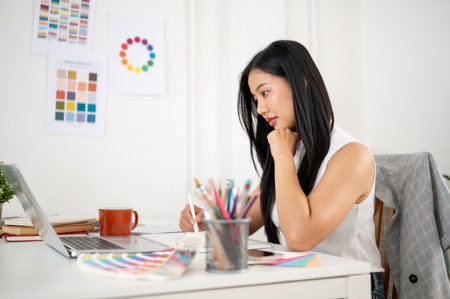 An asian woman is looking intently at the laptop screen while working on the design with graphic tablet. Interior Designer or Graphic Designer working in office.の写真素材