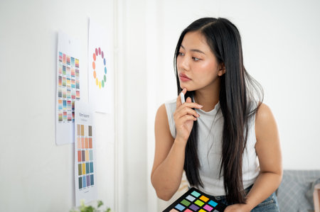 An asian woman is looking closely at a printed color palettes or a printed color wheel on the wall. Interior Designer or Graphic Designer working in office.の写真素材