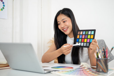 An asian woman is looking excited while showing a color palette to her client or her coworker in online meeting, Interior Designer or Graphic Designer in office.の写真素材