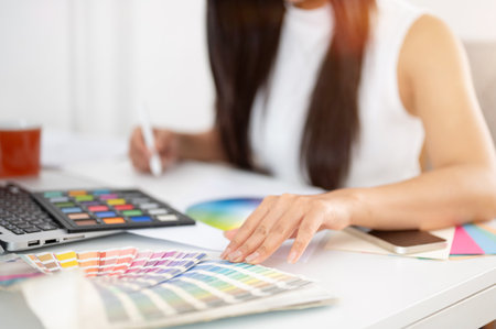 Close up of a hand touching on printed color charts and other hand holding a stylus drawing on tablet. Interior Designer or Graphic Designer working in office.の写真素材