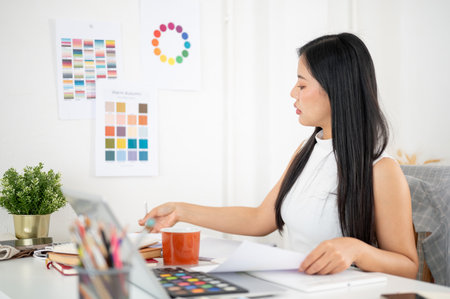 An asian woman is finding or sorting the documents on her working table. Interior Designer or Graphic Designer working in office.の写真素材