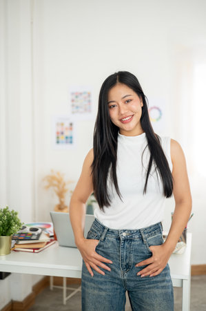 An asian woman is smiling while standing and posing in front of her work desk with working materials. Interior Designer or Graphic Designer working in office.の写真素材