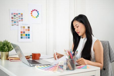 Asian woman is drawing or making a design on a graphic tablet while reading documents. Interior Designer or Graphic Designer woking in office.の写真素材