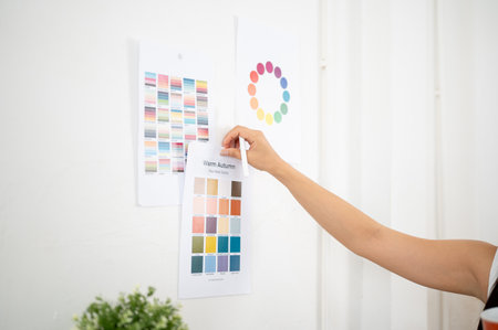 Close up of a hand sticking or taking off a printed color palette on the wall while holding a stylus. Interior Designer or Graphic Designer working in office.の写真素材