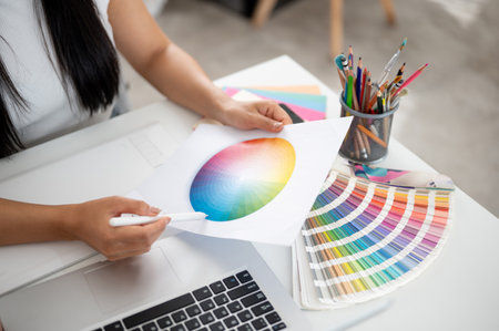 A close up of a pair of hand holding a printed circle color chart and a stylus pointing at the blue color on working table. Interior Designer or Graphic Designer in office.の写真素材