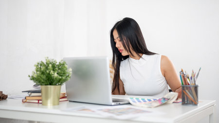 An asian woman is looking at the printed colour charts or colour palette documents on the table. Interior Designer or Graphic Designer working in office.の写真素材