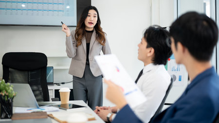 Female office worker is showing and explaining the datas on monitor to her male coworkers. Businessman and businesswoman is having a meeting in office.の写真素材