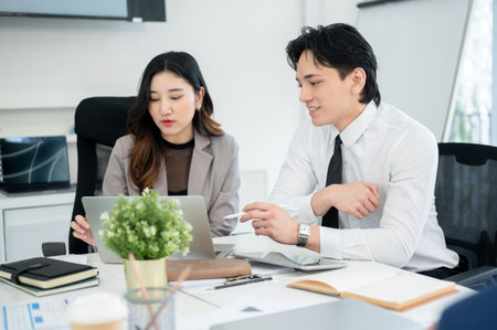 Male office worker is smiling while looking at the laptop screen of his female coworker. Businessman and businesswoman is having a discussion in the office.の写真素材