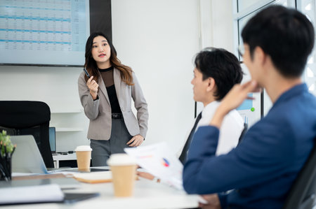 Female office worker is holding a pen while talking to her male coworkers. Businessman and businesswoman is having a meeting in office.の写真素材