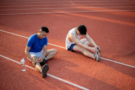 Two asian athlete men stretching their legs muscles together on the racetrack. Jogging or Running, Outdoor exercise or work out, Sport and health.の写真素材