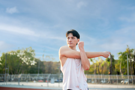 An asian man in white tank top stretching his arm and shoulder muscles on racetrack. Jogging or Running, Outdoor exercise or work out. Sport and health.の写真素材