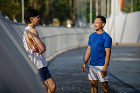 Two asian men or male friends are smiling while talking together at sports stadium fence or railing. Outdoor exercise or work out, Athlete training.の写真素材