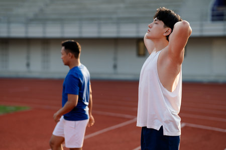 Two asian athlete men are standing leisurely on the racetrack in sports stadium. Taking a rest or relaxing, Outdoor exercise or work out.の写真素材