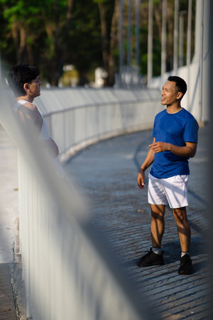 Two asian men or male friends are talking together while standing at sports stadium fence or a railing. Outdoor exercise or work out, Athlete training.の写真素材