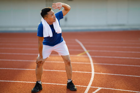 Asian man in blue t shirt standing with hands on his knee and looking up with hand on his eyes. taking a rest after running. Outdoor exercise or training.の写真素材