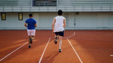 Two asian athlete men or male friends are running together on the racetrack in sports stadium. Athlete training, Outdoor exercise or work out.の写真素材
