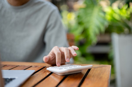 Close up of a hand using a white calculator on wooden table while sitting in a cafe or coffee shop. Study or working outdoor.の写真素材