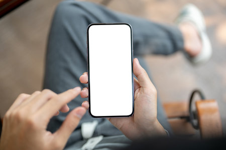 A hand holding smartphone with finger pointing at the white screen, sitting cross legged on chair. Empty screen mock up, Product display, Advertisement.の写真素材