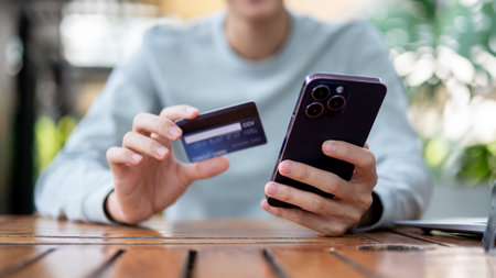 A man holding smartphone and other hand holding a credit card while sitting at wooden table in the cafe or coffee shop. Bank advertisement, Bill payment.の写真素材