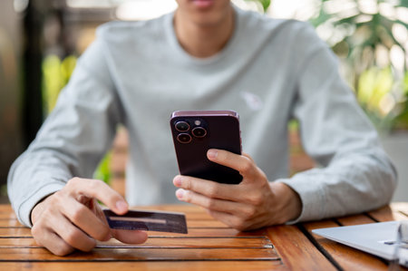 A man holding smartphone and other hand holding a credit card while sitting at wooden table in the coffee shop cafe. Bank advertisement, Bill payment.の写真素材