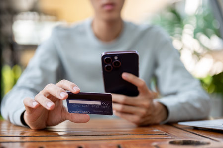 A man holding smartphone and other hand holding a credit card while sitting at wooden table in the cafe or coffee shop. Study or working outdoor.の写真素材