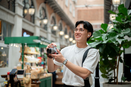 Asian man wearing glasses in white tee is looking around and taking a photo on his camera in...