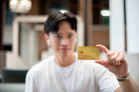 Asian man wearing glasses in white t shirt holding or showing a yellow credit card. Card payment,...