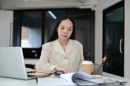 Businesswoman or female office worker is reading documents while sitting at working table in the...