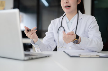 Close up of a female doctor with stethoscope holding pen and explaining while sitting at white table in diagnosis room, Hospital or Clinic office.の写真素材