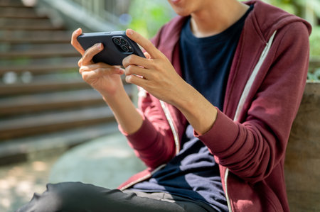 An asian man is watching videos or playing games on smartphone holding horizontally with both hands...
