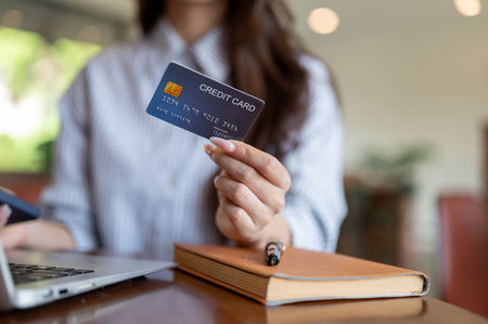 Close up of blue shirt woman holding or showing a credit card while sitting with laptop at wooden table in cafe. Cashless payment.の写真素材