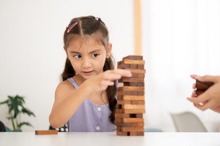 Asian kid or a little girl in purple shirt is looking closely while pull out a block from a wooden tower on table in white room. Kids toys, Wooden blocks.の写真素材