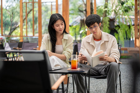 Asian woman looking or reading a notebook in a man hands while sitting together at folding table. Working or Study outdoor, Garden Cafe or Restaurant.の写真素材