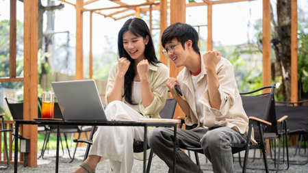 Asian woman and a male friend looking at laptop with a happy or an excited face at folding table. Working or Study outdoor, Garden Cafe or Restaurant.の写真素材