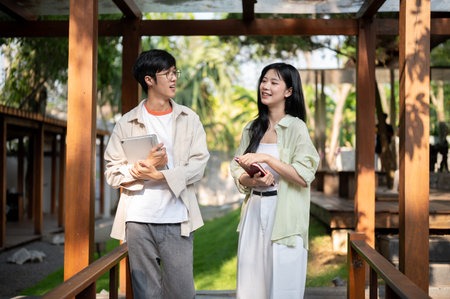 Smiling asian man is talking to his female friend and standing together in the wooden corridor. Working or Study outdoor, Garden Cafe or Restaurant.の写真素材