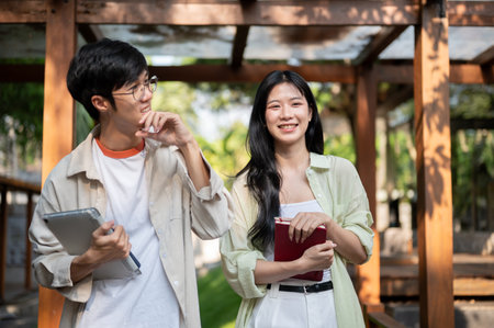 Asian friends or a couple of man and woman are laughing while walking together in wooden corridor. Working or Study outdoor, Garden Cafe or Restaurant.の写真素材
