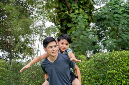 Father carrying a son playing airplane on his back after playing together in their backyard or a park. Going Outdoor, Family bonding, Sports activity.の写真素材