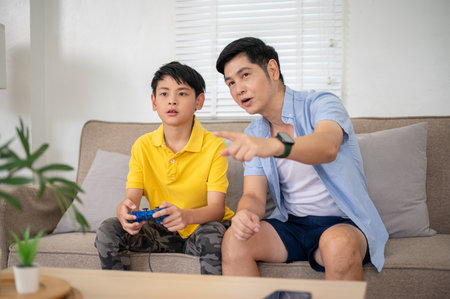 Asian father teaching elementary school son holding a joystick or controller to play video game at...