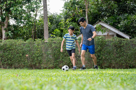 Father and son having fun in playing soccer together in their home's backyard or green grass field. Man and boy, Family bonding, Sports activity.の写真素材