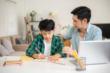 Father is talking or praising his son while his son doing a homework at table in their house. Elementary Schoolboy, Kids education, Family bounding.の写真素材