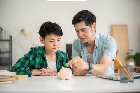 Father teaching his son to save money while putting a coin in pink piggy bank. Elementary Schoolboy, Kids education, Family bonding, money management.の写真素材