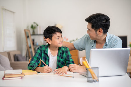 Father and son smiling at each other while teaching and doing homework together in the house....