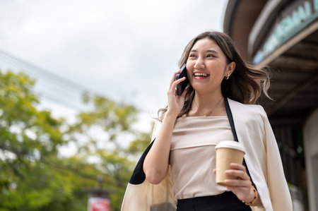 Close up of long hair asian woman smiling while talking on the phone in front of a building with coffee cup in her hand. Urban Life, Chilling Outdoor.の写真素材