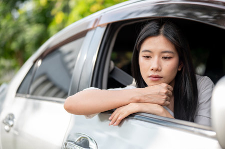 Asian woman in white shirt looking bored or tired in driver seat of a car parked at parking lot or roadside. Picking up friend or Waiting for family.の写真素材