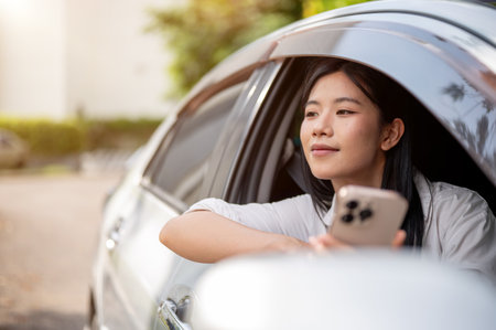 Asian woman in white shirt looking away from phone inside a car parked at parking lot or roadside....