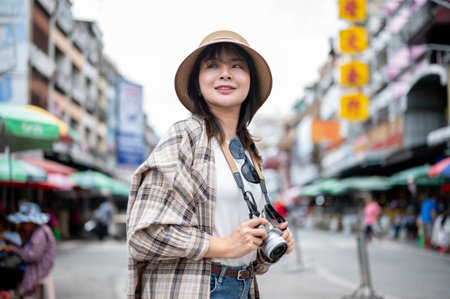 Asian tourist woman wearing hat looking and around while holding a camera standing by the road of local market. Walking street, Old town trip.の写真素材