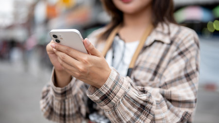 Close up of a tourist woman in a pattern shirt holding a smartphone while standing by the road in a local market. Walking street, Old town trip.の写真素材